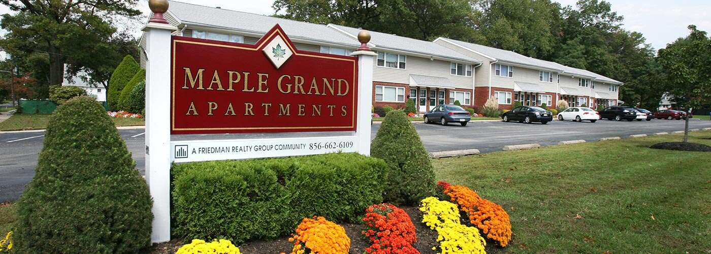 Sign outside of Maple Grand Apartments surrounded by fresh landscaping and beautiful mums