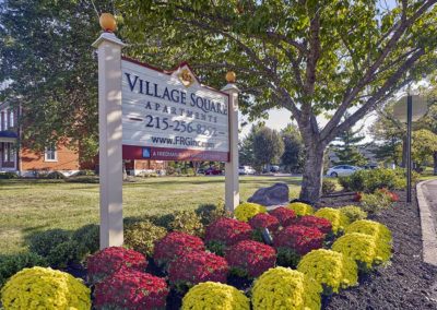 Village Square Apartments property sign surrounded by beautiful landscaping