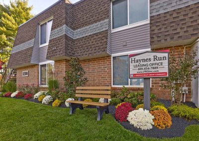 Exterior of Haynes Run Apartments' leasing office with a bench and lush landscaping