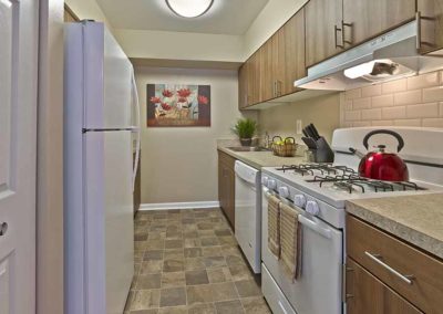 Beautifully renovated galley kitchen with stone tile flooring, brown cabinetry, and white appliances