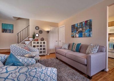 Furnished living room with blue accents and neutral colored couch with closet and stairs leading to second floor