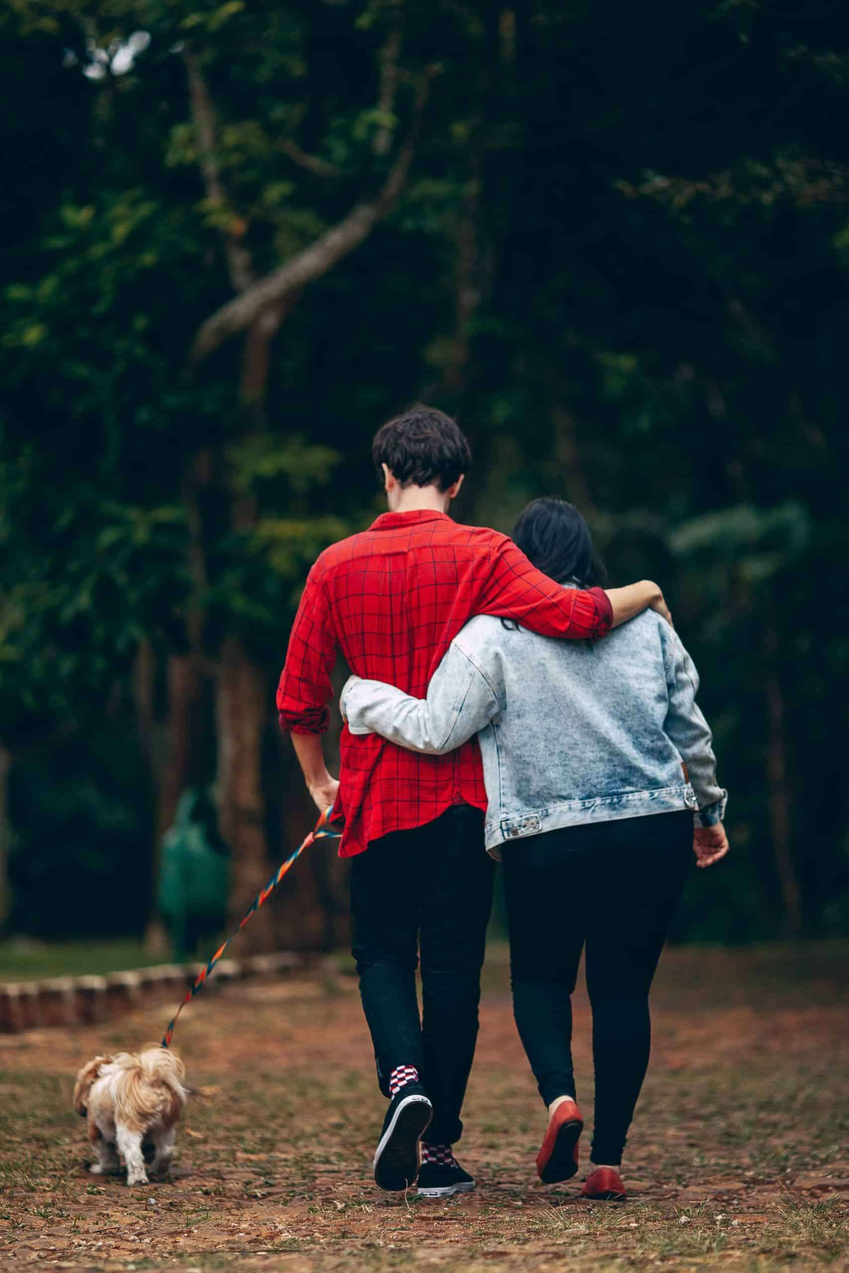 couple with arms around each other walking dog in woods