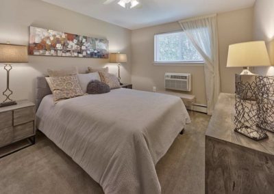 Furnished master bedroom with neutral colored furniture and queen sized bed below ceiling fan and in front of small window