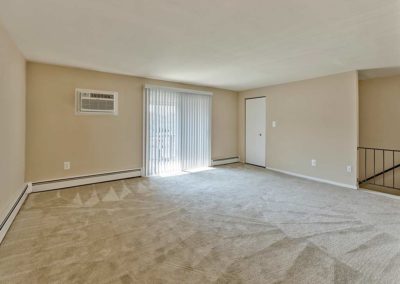 Large carpeted living room with staircase on right side and sliding glass doors out to balcony