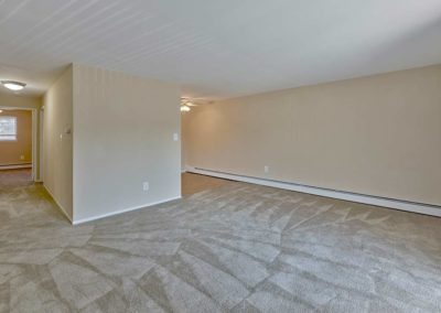 Large living room with carpeting and neutral colored walls leading into a hallway