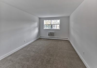 Large apartment bedroom with plush carpeting, a sunny window, and a personal air conditioning unit