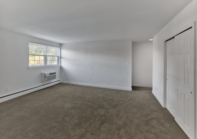 Spacious living area with large window, baseboard heating, and plush carpeting