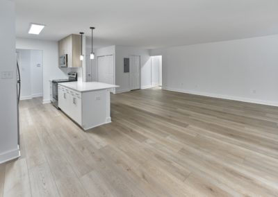 Unfurnished, open concept floor plan with plank flooring and a modern kitchen with a breakfast bar