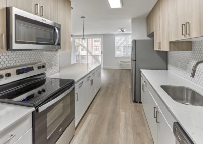 Renovated kitchen with quartz countertops, white tiled backsplash, and stainless steel appliances