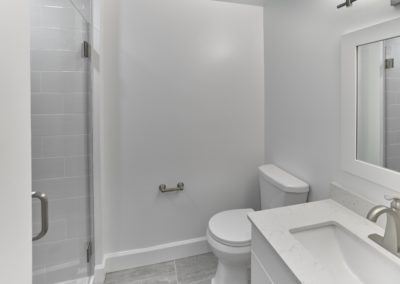 Bathroom with grey tile flooring, a single sink vanity, toilet, and walk-in shower